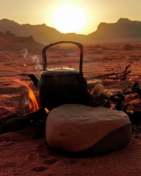 A teapot on a small fire as the sun sets behind the mountains