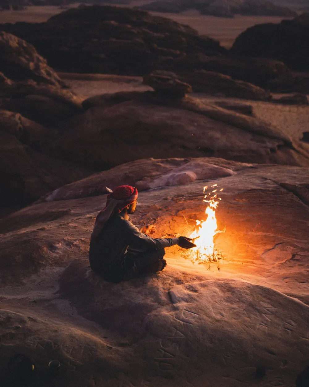 A Bedouin man sitting by a small fire on the rocks at dusk