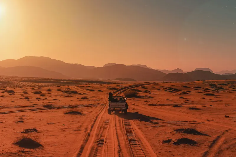 A jeep driving along a sand track toward the setting sun